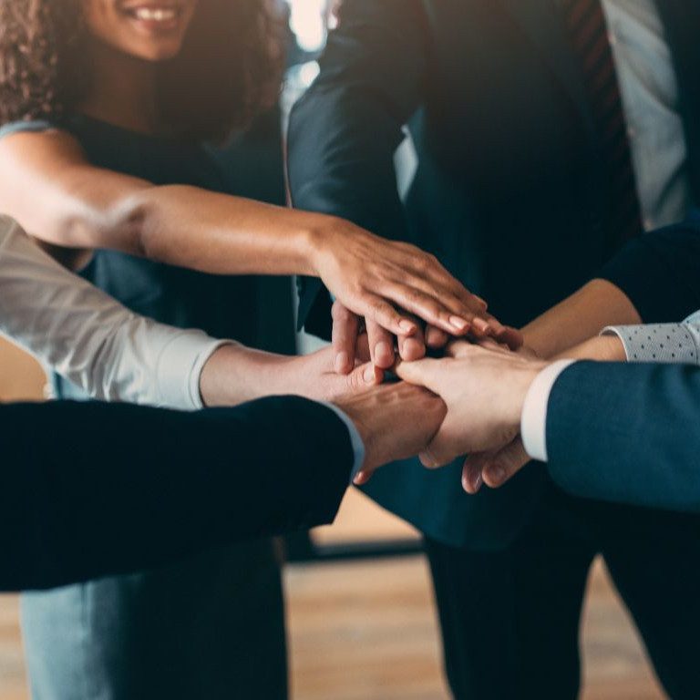 Small group of office people celebrating teamwork with a group handshake.